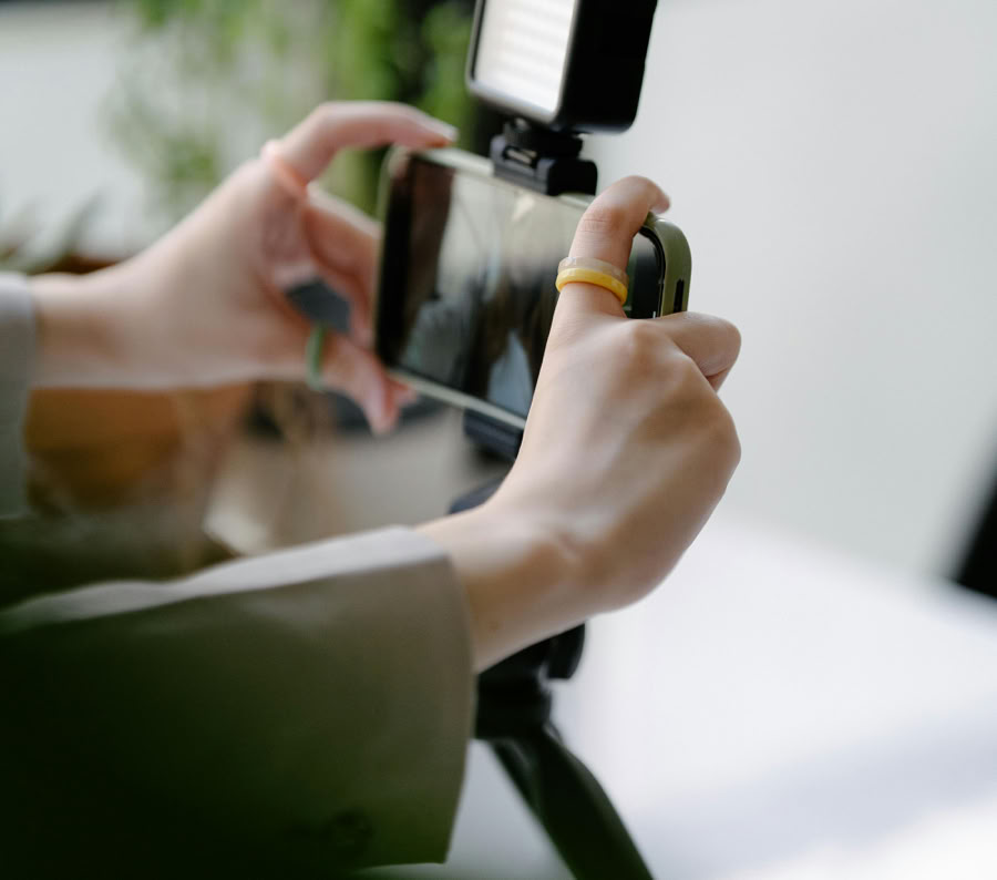 Close-up of hands operating smartphone on a tripod with LED light indoors.